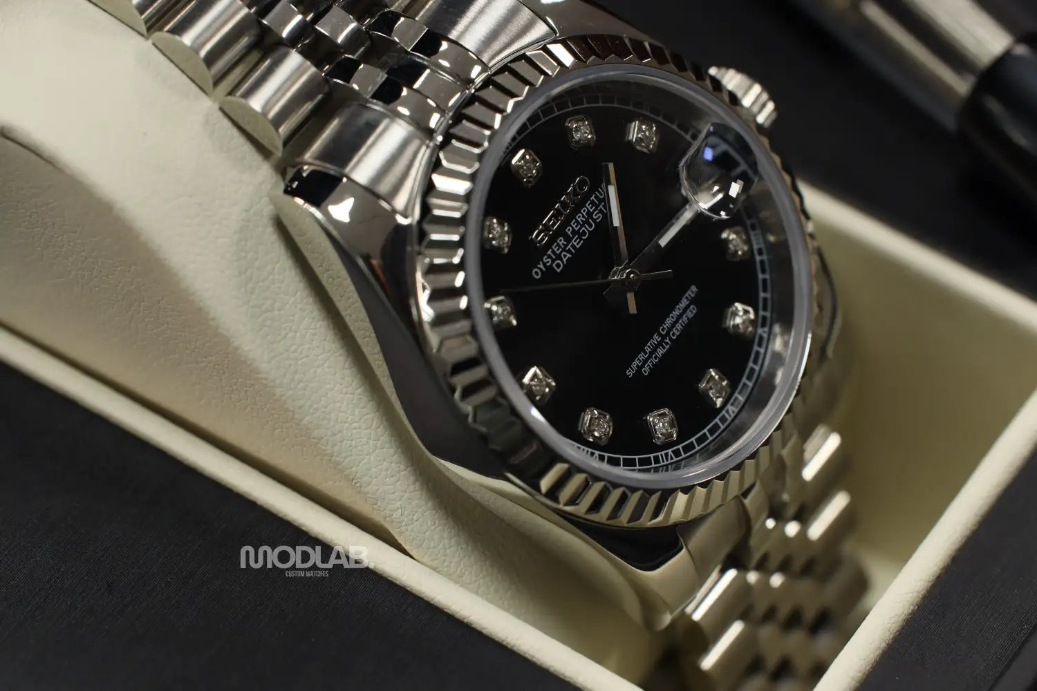 A sleek silver seiko oyster perpetual watch with a black dial adorned by diamond hour markers and a fluted bezel, nestled in its presentation box.