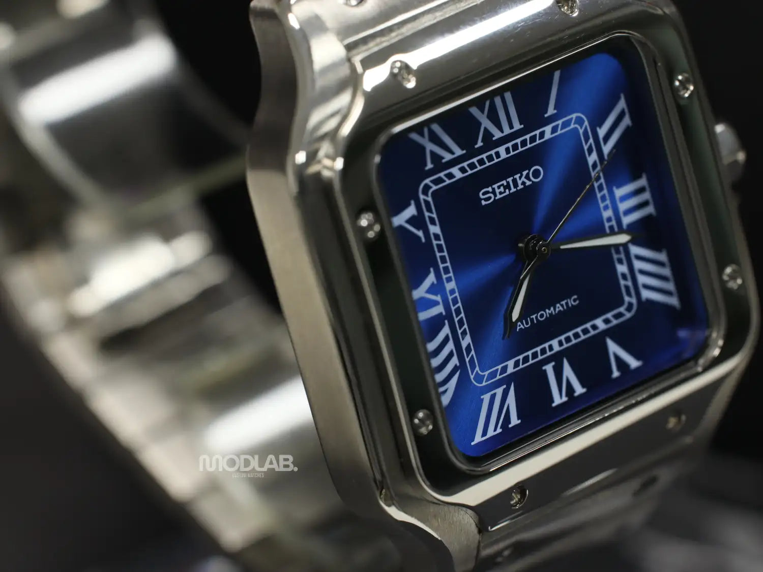 Silver-toned seiko automatic watch with a square case and blue dial featuring white roman numerals.