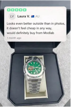 Silver-toned watch with a vibrant green dial and visible mechanical movement, housed in an elegant rectangular box.