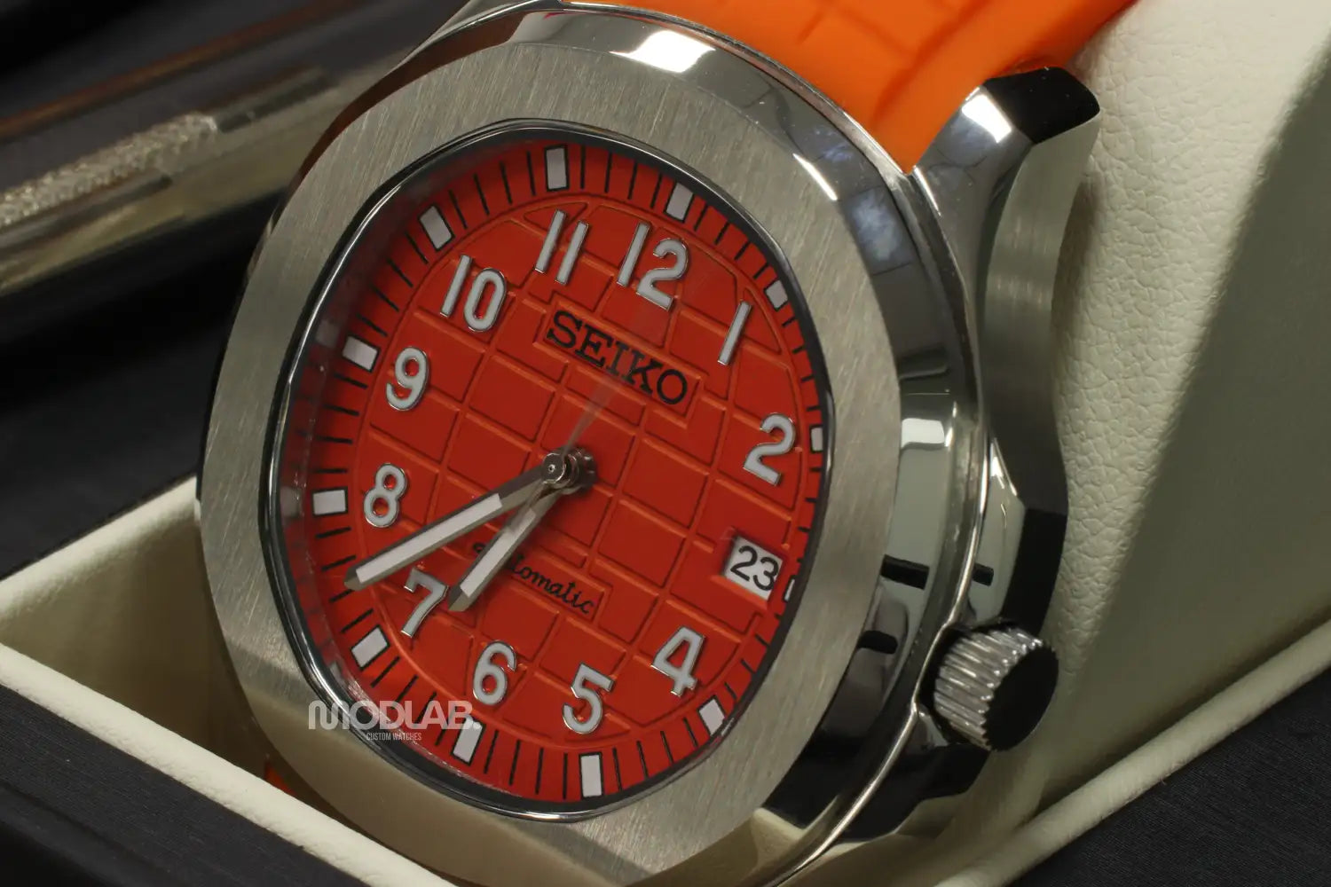A vibrant orange seiko automatic watch with a stainless steel case and matching dial, featuring bold white numerals and a textured grid pattern.